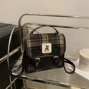 Vista dettagliata della borsa in lana a quadri con toppa di orso vintage e fibbie in pelle