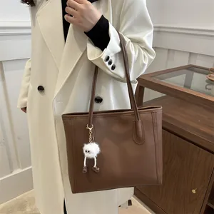 Dettaglio di una borsa tote in pelle PU marrone con ciondolo in peluche e spalline sottili