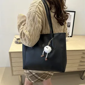 Dettaglio borsa tote nera in similpelle con ciondolo peluche bianco sulla spalla della modella