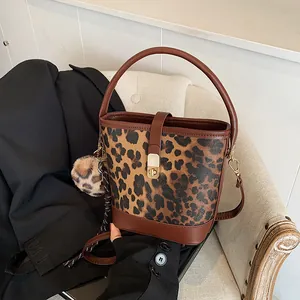 Detail der modischen Leopard-Eimertasche mit Goldverschluss und Plüsch-Anhänger auf Sofa