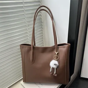 Dettaglio della borsa tote marrone caffè con ciondolo a mostro in peluche su libri