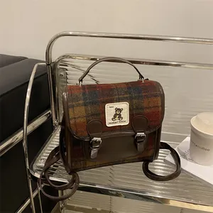 Dettaglio ravvicinato di borsa in lana a quadri con bordi in pelle retro e patch orso