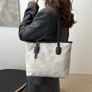 Detail of grey marbled tote bag with golden logo and black shoulder straps shown on model