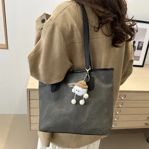 Detail of dark grey textured tote bag with gold lettering and white plush doll pendant