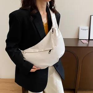 Close-up of white leather crescent crossbody bag with black metal zippers worn by model