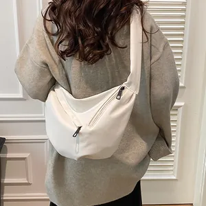Minimalist white leather crescent crossbody bag shown on a model wearing a grey sweater