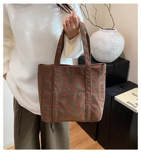Détail du sac fourre-tout en velours côtelé marron à imprimé cerise porté par un modèle