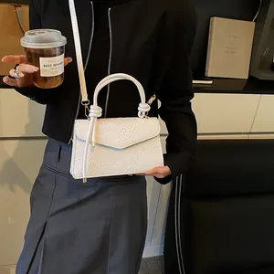 Close-up of white crossbody bag with floral embossing and elegant cylindrical handle