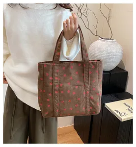 Detail of a brown corduroy tote bag featuring strawberry embroidery and outer pocket