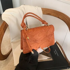 Detail of koi fish and lotus embossing on orange-brown handbag with knotted handle