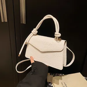 Macro shot of white embossed lotus pattern on PU leather handbag with gold hardware