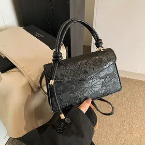 Detail of black crossbody bag with embossed koi and lotus patterns and top handle