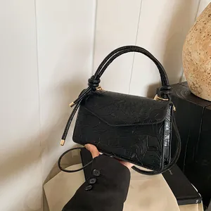 Detail of black embossed PU leather handbag featuring lotus and fish patterns