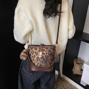 Detail view of leopard print bucket bag with gold clasp and furry pompom charm