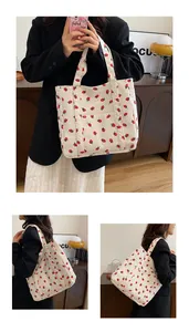 Detail of white corduroy tote bag featuring red strawberry print and front pocket sleeve