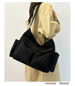 Dettaglio della grande borsa a tracolla in tela nera con tasche frontali multiple su modella