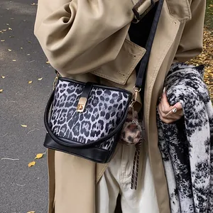 Detail of leopard print bucket bag with gold twist lock and fuzzy ball charm on model