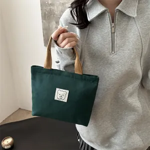 Détail du sac en toile verte avec anses tissées marron et étiquette d'ours mignon