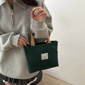 Détail du sac en toile vert foncé avec patch ours et poignées tissées marron