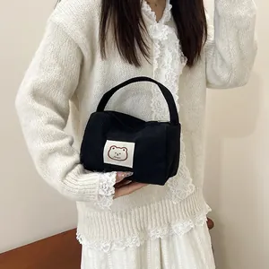 Detail of black corduroy handbag featuring a cute cartoon bear patch and zipper closure