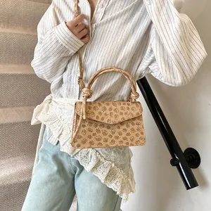 Detailed view of beige clover print crossbody bag featuring twisted handle and envelope flap