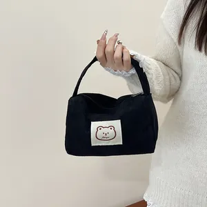 Detail of black corduroy handbag featuring a cartoon bear patch and top zipper closure