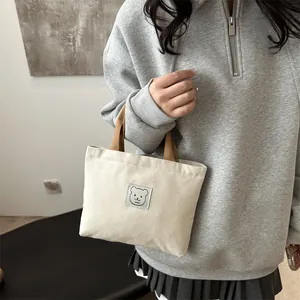 Détail du sac cabas en toile montrant l'écusson d'ours et les poignées marron