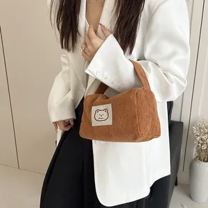 Close-up of brown corduroy handbag featuring a cartoon bear label on white blazer