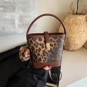 Detail of leopard print bucket bag with metal twist lock and plush pompom charm