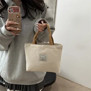 Détail d'un mini cabas en toile avec anses marron et motif d'écusson d'ours mignon