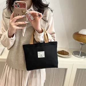 Détail du sac cabas en toile noire avec anses marron et écusson ours mignon