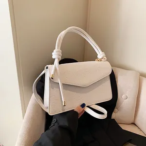Detail shot of white small square handbag featuring embossed clover pattern and gold hardware