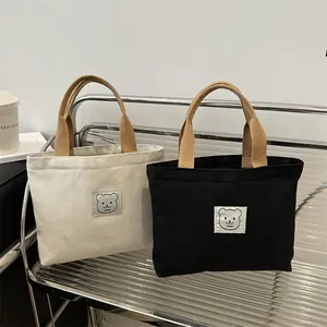 Détail de sacs en toile avec poignées tressées et écusson ours sur étagère en métal