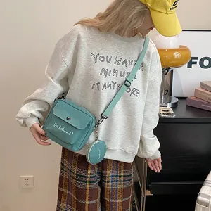 Detail shot of a teal canvas crossbody bag with white lettering and round mini purse