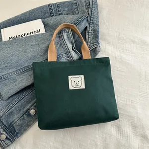 Détail d'un sac cabas en toile verte avec patch ours brodé et anses tissées marron