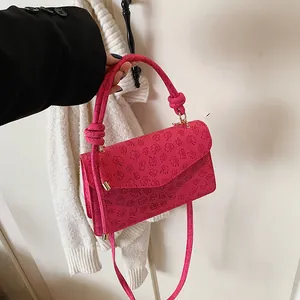 Detail of rose red crossbody bag with embossed clover patterns and knotted handle