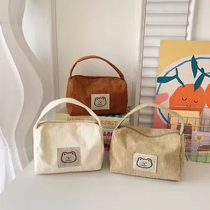 Detailed view of three corduroy cosmetic bags in beige, tan and khaki with bear patch