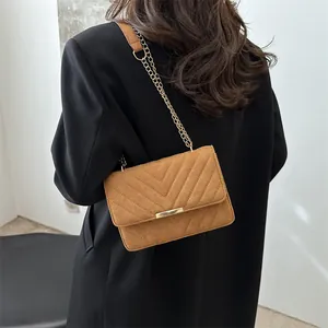 Detailed close-up of brown suede crossbody bag with V-quilt pattern and gold chain strap