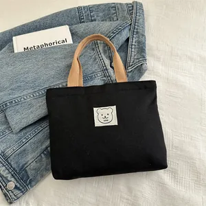 Détail d'un sac en toile noir avec écusson ours mignon et poignées beige clair