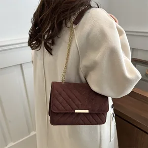 Detail of a dark brown suede crossbody bag with V-shaped quilting and a gold metal chain