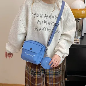 Close-up of blue canvas crossbody bag set with small round coin purse and white text logo