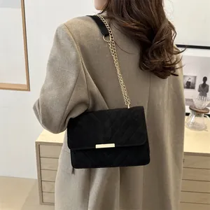 Detail of black V-quilted crossbody bag with gold chain strap on camel blazer