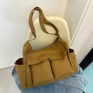 Dettaglio di una grande borsa a tracolla in tela marrone con tasche su sedia beige