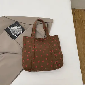 Close-up of brown corduroy tote bag with strawberry patterns and a front pocket