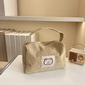 Detail of corduroy makeup bag with cute bear patch and zipper closure on a white desk