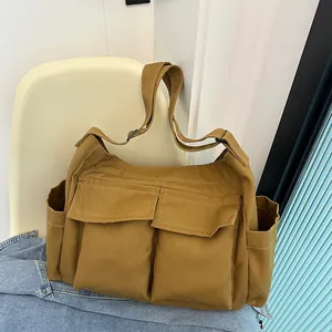 Dettaglio della borsa a tracolla in tela kaki con due tasche frontali su sedia bianca