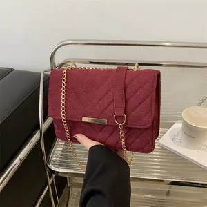 Close-up of burgundy suede shoulder bag with V-quilted pattern and golden chain strap