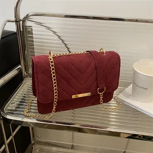 Detail of burgundy chevron quilted crossbody bag with golden chain strap on a shelf