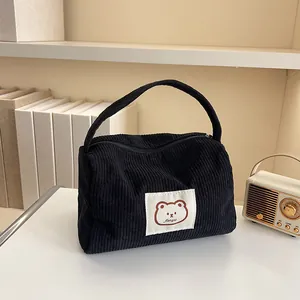 Detail of black corduroy makeup bag featuring a cute bear patch and sturdy top handle