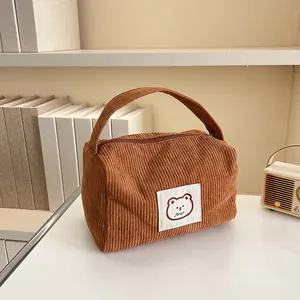 Detail view of brown corduroy cosmetic bag with a cute bear patch on a minimalist desk